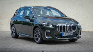 Dunkelgrüner BMW 230e steht vor gelber Hauswand und ist von schräg vorn, leicht von oben fotografiert