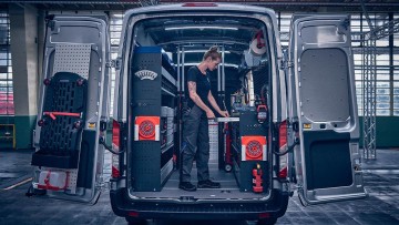 Geöffnete Flügeltür am Ford Transit mit darin stehender Mechanikerin die Werkzeuge aus der integrierten Werkbank entnimmt