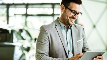 Automobilverkäufer steht mit einem Tablet in der Hand in einer Fahrzeugausstellung