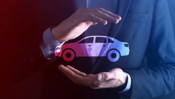Symbolbild für das Thema Fahrzeuggarantie - ein Mann hält schützend seine Händler um ein Auto-Piktogramm