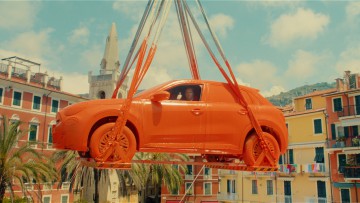 Ein in Orange getauchter Fiat hängt an einem Kran.