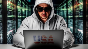 EIn Hacker sitzt vor einem Notebook mit einem Aufkleber USA.