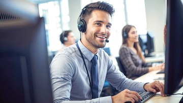 Mann mit Headset sitzt am Schreibtisch mit Bildschirmen