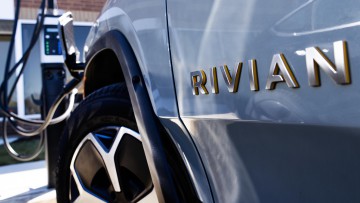 Ein Rivian-Logo ist an einem Fahrzeugmodell zu sehen, das an einer Ladestation steht