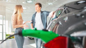 Eine Frau und ein Mann stehen an einem Elektroauto in einem Autohaus.