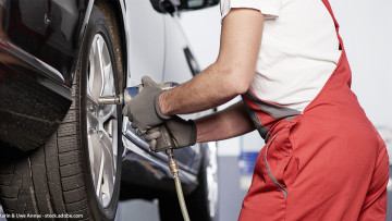 Mechatroniker wechselt einen Reifen mit einem Schlagschrauber an einem Auto das auf einer Hebebühne steht