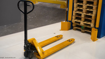 Ein Hand-Gabelhubwagen steht vor einem Stapel Holz-Paletten.