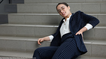 Eine Frau sitzt auf einer Treppenstufe und hält sich mit schmerzverzerrtem den Rücken, da sie gestürzt ist.