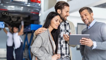 Serviceberater zeigt jungem Pärchen in der Werkstatt etwas auf dem Tablet