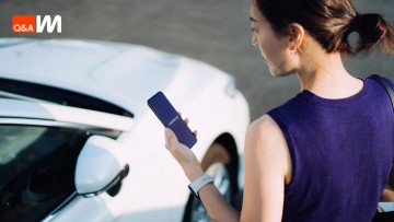 Frau schaut aufs Handy vor Auto