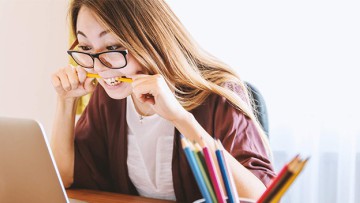 junge Frau vor Laptop in einen Bleistift beißend