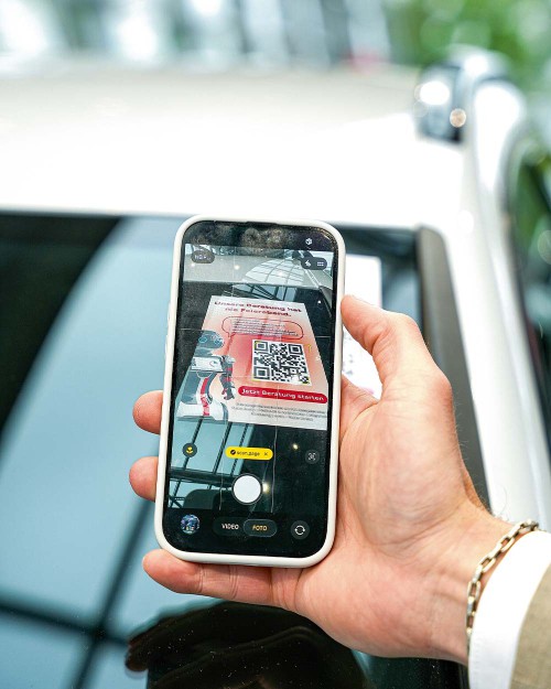 Ein Kunde scannt mit dem Smartphone den Evo.Rep QR-Code an einem Fahrzeug, um den Dialog mit dem Bot zu starten