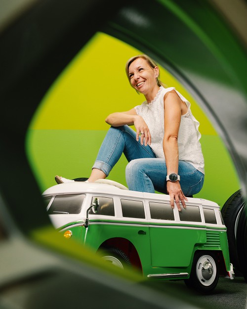 GETTYGO-Mitarbeiterin sitzt lachend auf einem Spielzeugmodell eines VW Bulli