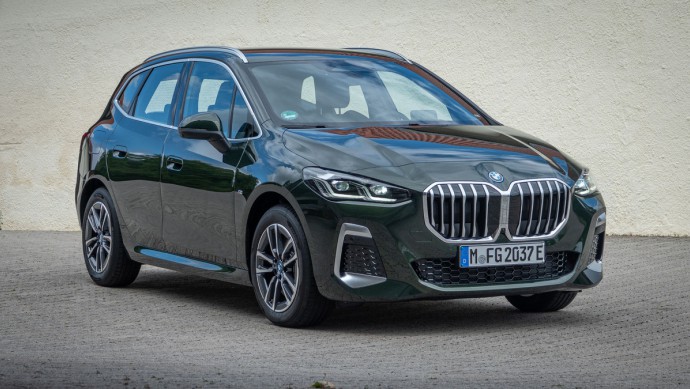BMW 230e xDrive Active Tourer Dunkelgrüner BMW 230e steht vor gelber Hauswand und ist von schräg vorn, leicht von oben fotografiert