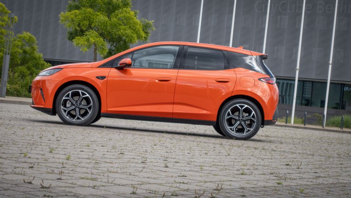 Orangefarbener BYD Dolphin G stehend auf einem großen Platz vor einem grauen Lagerhaus.