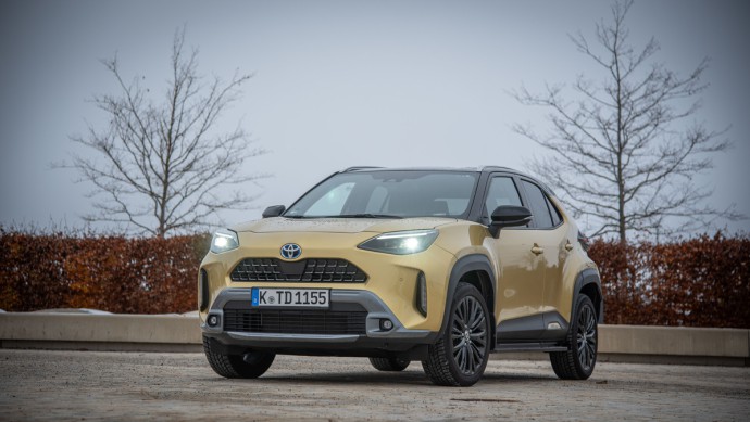 Toyota Yaris Cross Hybrid AWD in goldgelb lackiert auf freiem Platz von schräg von fotografiert