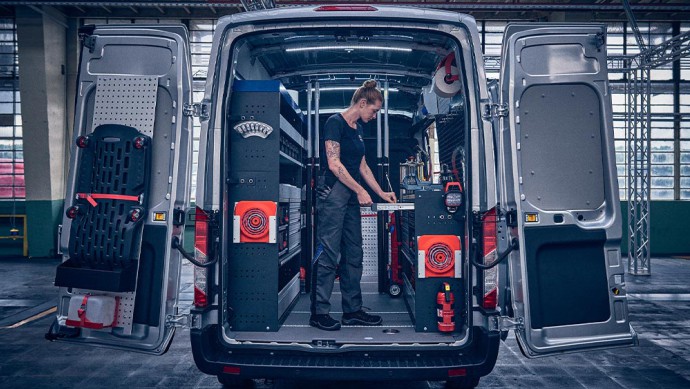 Geöffnete Flügeltür am Ford Transit mit darin stehender Mechanikerin die Werkzeuge aus der integrierten Werkbank entnimmt