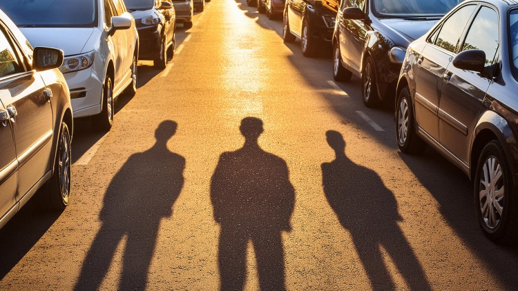 Die Schatten von 3 Männern sind im Gegenlicht zwischen vielen Autos zu sehen