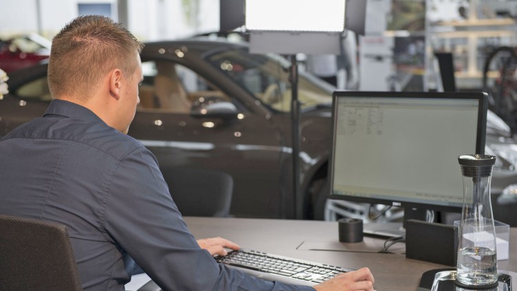 Ein Automobilkaufmann sitzt an einem Schreibtisch in einem Autohaus