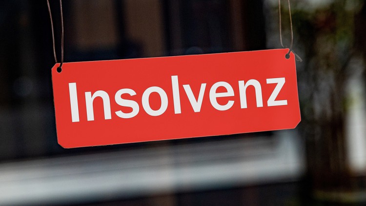 Ein symbolisches, rotes Schild mit der Aufschrift "Insolvenz" hängt leicht schräg an Bändern in einem Schaufenster.