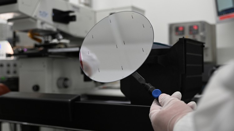 Ein Mitarbeiter der Nexperia Germany GmbH hält ein Zwischenprodukt der Halbleiterproduktion, einen sogenannten Wafer, in den Räumlichkeiten des Halbleiterproduzenten Nexperia mit einer Pinzette fest.