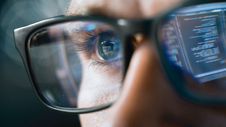 Mann mit Brille, in dem sich ein Computer-Monitor spiegelt