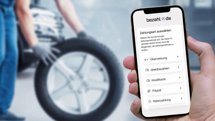 Smartphone mit bezahl.de App und Mechaniker beim Reifenwechsel