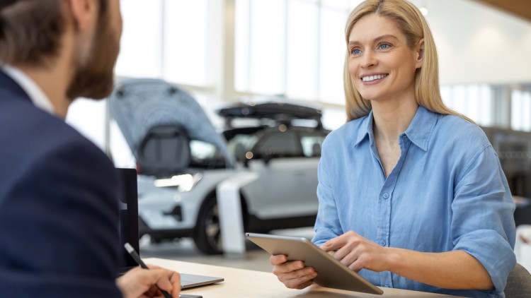 Autoverkäufer und Kundin sitzen im Autohaus am Schreibtisch