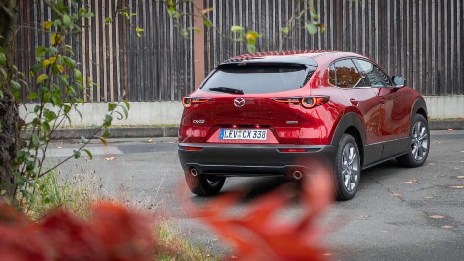 Heckansicht eines roten Mazda CX-30 vor einer Holzwand auf Asphalt stehend