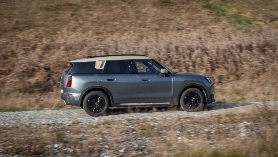 Mini Countryman D (U25) fahrend vor einer Graswand von links nach rechts in der Morgensonne