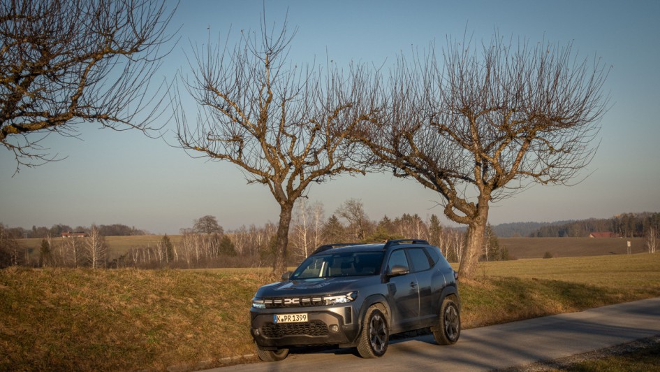 Dacia Duster von vorn fotografiert vor kahlen Bäumen im Winter mit goldgelber Sonne