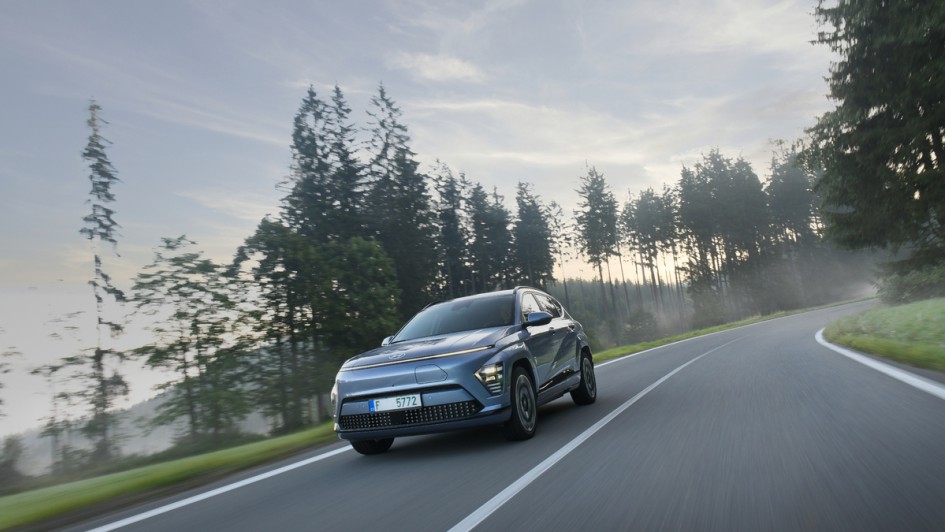Hyundai Kona-e von vorn fahrend auf Landstraße mit Bäumen am Rand